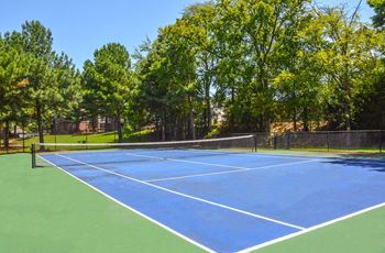 A blue tennis court surrounded by trees.